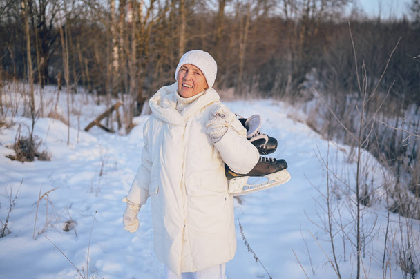 Mulher madura idoso feliz em roupas brancas quentes brincando com patins de gelo no inverno ensolarado neve ao ar livre. Pessoas saudáveis aposentadas férias atividades de inverno, conceito de estilo de vida ativo - Foto, Imagem