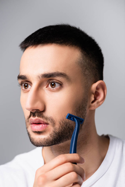 bearded hispanic man shaving with safety razor isolated on grey - Zdjęcie, obraz