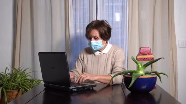 Femme âgée 70 ans avec masque dans l'appartement travailler et téléphone avec ordinateur portable dans l'appartement pendant Covid-19 Coronavirus verrouillage maison de quarantaine style de vie dans l'épidémie fin du temps libre - Séquence, vidéo