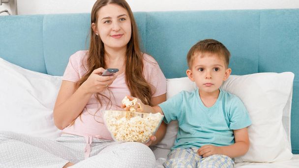 Portret rodziny w piżamie leżącej w łóżku z dużym popcornem i oglądającej film w weekendowy poranek - Zdjęcie, obraz