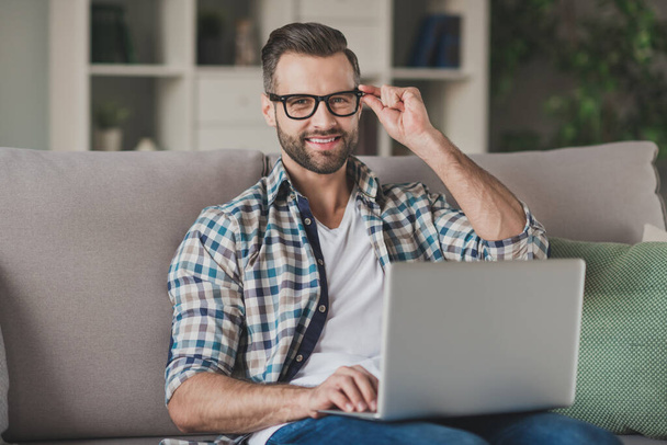 Photo of young handsome business man happy positive smile sit sofa home work distance browse laptop hand touch glasses - Φωτογραφία, εικόνα