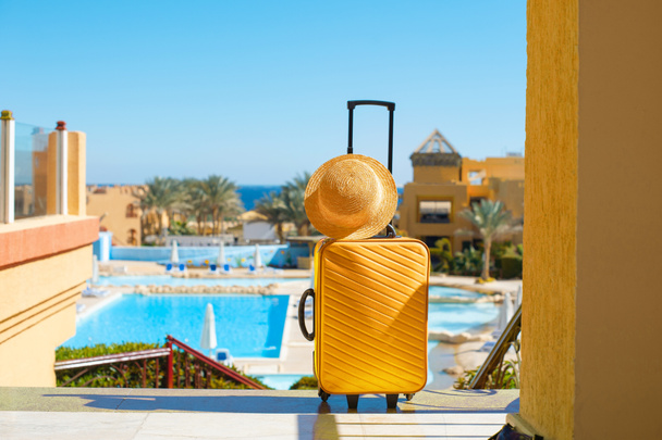 Viajes, vacaciones de verano y el concepto de vacaciones maleta amarilla con sombrero en el fondo de la zona de la piscina del hotel en Egipto - Foto, imagen