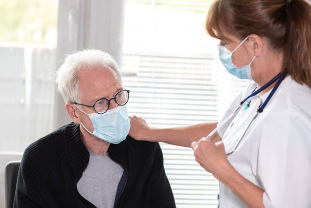 Médecin féminin aidant un homme âgé à porter un masque médical protecteur ; consultation médicale pendant une éclosion de coronavirus - Photo, image
