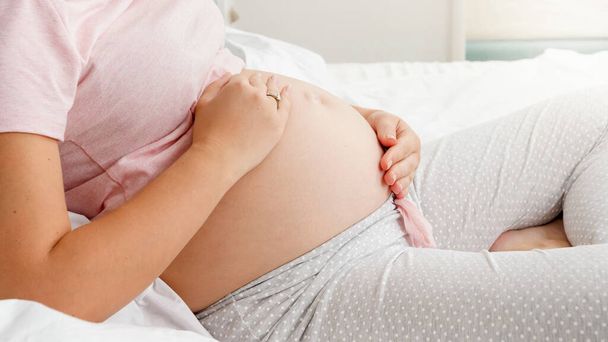 Zbliżenie kobiety w ciąży delikatnie głaskającej się po brzuchu. Koncepcja rodzicielstwa i szczęśliwego przewidywania przyszłego dziecka. - Zdjęcie, obraz
