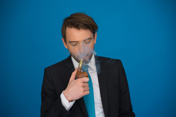 бизнесмен с электронной сигаретой в костюме и галстуке на синем
 - Фото, изображение