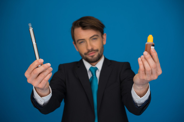 бізнесмен тримає електронну сигарету та електронну рідину на синьому
 - Фото, зображення