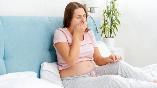 Mujer embarazada joven sintiéndose enferma descansando en la cama y tosiendo en la mano. Concepto de embarazo atención médica y examen médico. - Foto, imagen