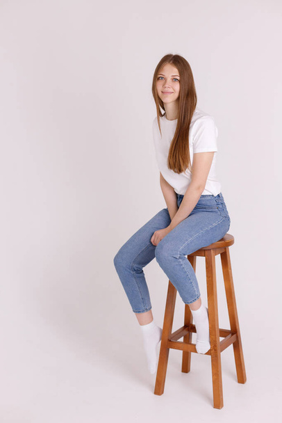 girl in a white T-shirt and blue jeans on a chair on an isolated background - Φωτογραφία, εικόνα