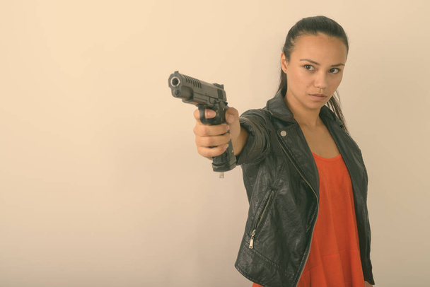 Зйомки молодої азіатської жінки з ручною вогнепальною зброєю на відстані проти білого фону. - Фото, зображення