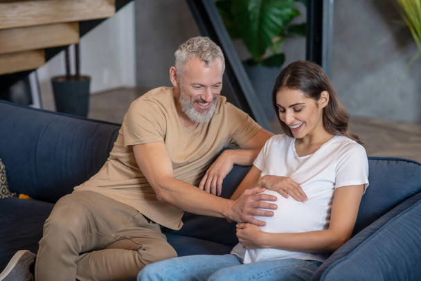 Happy mature man and young pregnant woman sitting and talking - Foto, imagen