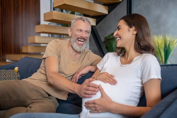 Happy mature man touching abdomen of his young pregnant wife and looking happy - Φωτογραφία, εικόνα