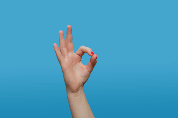 жінка показує нормальний жест. Жіноча рука з манікюром з червоного гелю на синьому фоні. Копіювати простір
 - Фото, зображення