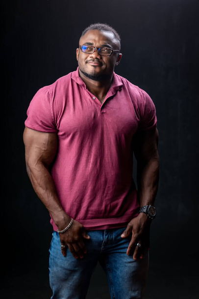 African american bodybuilder stands with hands in pockets on black studio background. Fashion model male. - Foto, imagen