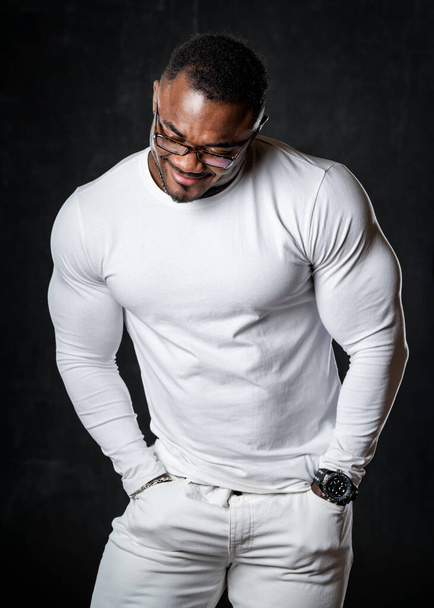 Ισχυρή σπορ afroamerican με μεγάλους μυς θέτει στην κάμερα σε ολόλευκη εμφάνιση. Σποραδικό υγιές σώμα. Πρόσθια όψη. - Φωτογραφία, εικόνα