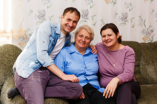 Dospělí usměvaví vnuci objímají starší babičku, rádi vidí, že jí chybí, návštěva milujících příbuzných se těší komunikaci, mazlit se jako symbol spojení, lásky a podpory konceptu - Fotografie, Obrázek