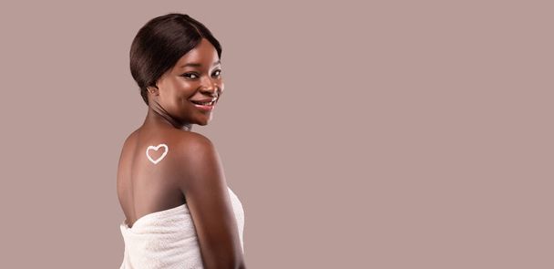 Mooie zwarte vrouw met hart gemaakt van lichaam crème op haar rug - Foto, afbeelding