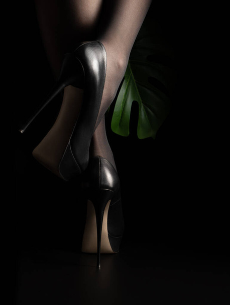 黒の背景にハイヒールの靴の女性の足. - 写真・画像