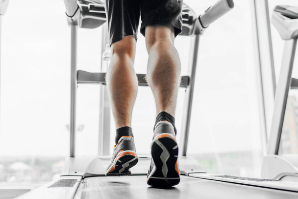 The focus is on men's legs running on a treadmill. - Fotó, kép