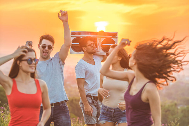 Os amigos felizes com uma caixa de boom dançando no fundo do sol brilhante - Foto, Imagem