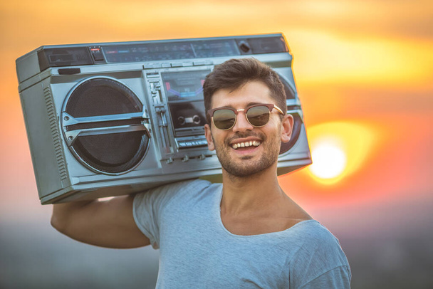 The handsome man stand with a boom box on the background of the sunset - 写真・画像