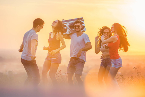 Οι πέντε χαρούμενοι φίλοι που χορεύουν με ένα κασετόφωνο στο φόντο του ήλιου - Φωτογραφία, εικόνα