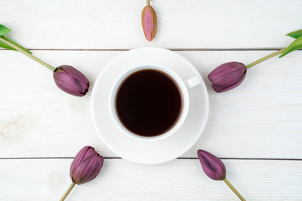 Flores de tulipán alrededor de una taza de café sobre un fondo claro. Vista superior con espacio para copiar. - Foto, imagen