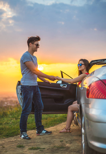 De gelukkige man staan in de buurt van een vrouw in cabrio op de felle zon achtergrond - Foto, afbeelding