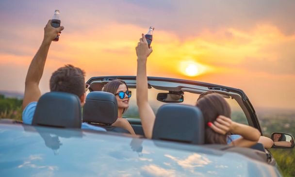The company of people sit in a cabrio on the sunset background - Photo, Image