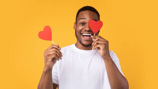 Cheerful Black Man Covering Eyes With Hearts Over Yellow Background - Photo, Image