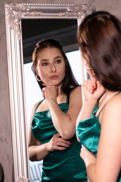 sexy atrakcyjna brunetka kobieta w eleganckiej zielonej sukni aquamarine przed lustrem. Piękna zmysłowa dziewczyna. przestrzeń kopiowania. - Zdjęcie, obraz