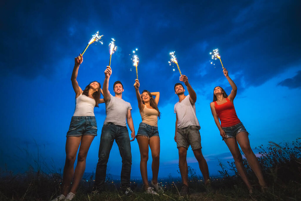 A boldog barátok tűzijátékbotot tartanak. esti időszámítás - Fotó, kép
