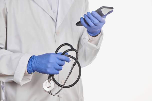 Physician holding a stethoscope and looking at a phone - Foto, afbeelding