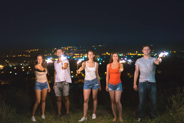 Przyjaciele trzymają fajerwerki na tle świateł miasta. wieczorna noc - Zdjęcie, obraz