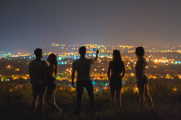 5人は街を背景に自撮りをする。夜の時間 - 写真・画像