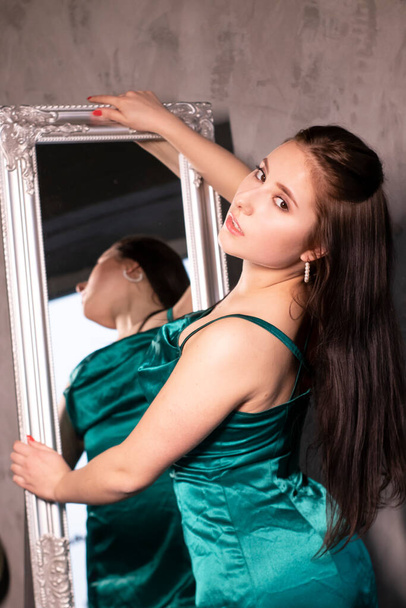 鏡の前のエレガントな緑のアクアマリンのドレスでセクシーな魅力的なブルネットの女性。美しい官能的な女の子。コピースペース. - 写真・画像