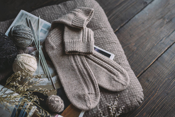 糸玉編みの針で手編みの靴下のペア。自然の色。暗い素朴な木製の背景.  - 写真・画像