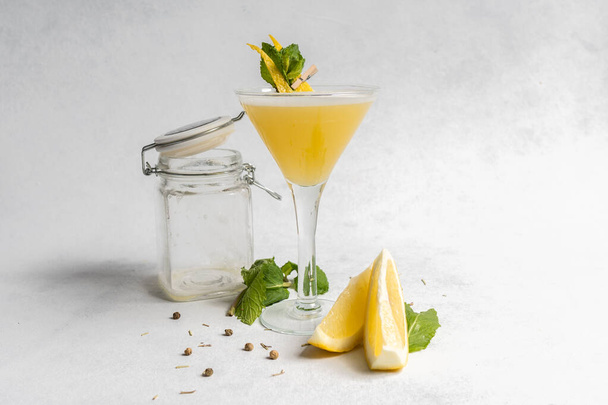 Cóctel amarillo fresco en una copa de martini con limón y menta - Foto, Imagen