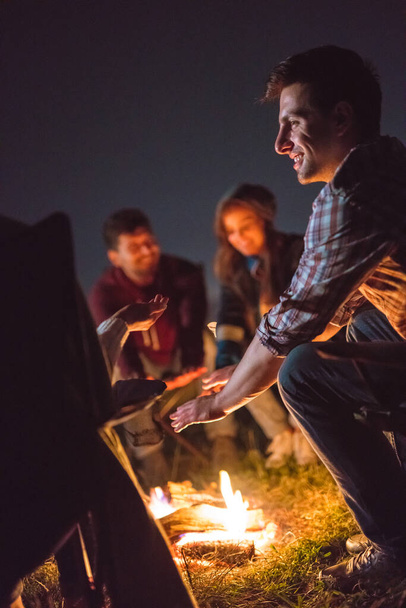 たき火の近くで手を暖める幸せな人々。夜の時間 - 写真・画像