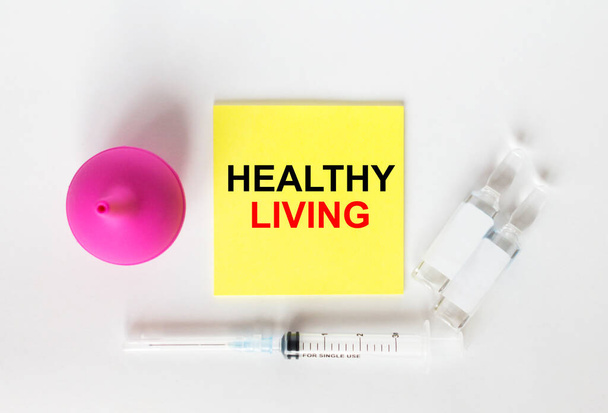 Yellow sticker with text Healthy Living on a white background with syringes, pills and ampoule. Medical concept photo - Φωτογραφία, εικόνα