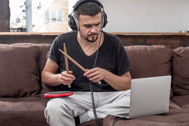 Mężczyzna gra na perkusji i patrzy na ekran laptopa. Koncepcja lekcji muzyki online, lekcje wideokonferencji. - Zdjęcie, obraz