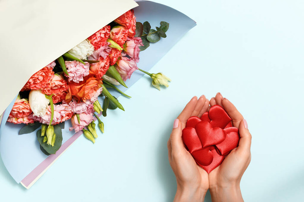 Top view of female hands with hearts and a bouquet of flowers on a blue pastel background. Valentine's day concept, symbol of love, romance. - Photo, Image