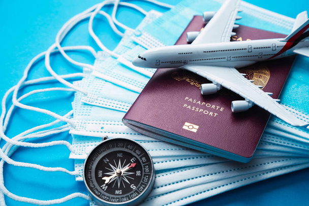 un avión comercial blanco encima de una máscara para covid-19 y un libro de pasaportes rojo cerca de una brújula de plata y un mundo - Foto, imagen