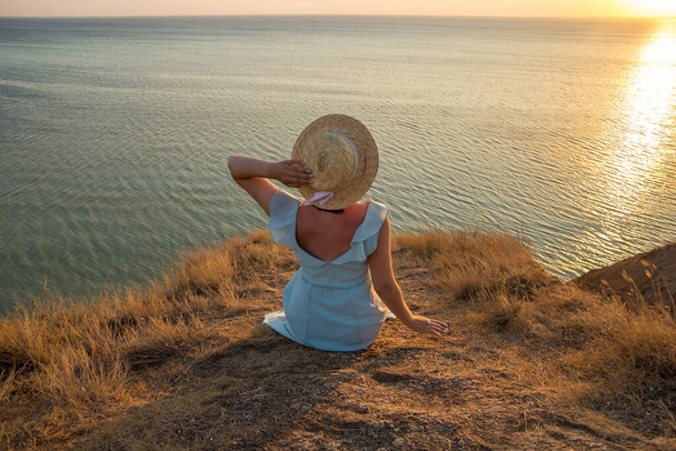 Tyttö mekossa ja hatussa istuu kalliolla meren rannalla. - Valokuva, kuva