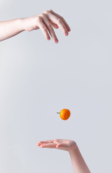 makea ja mehukas mandariini putoaa yhdestä kädestä lapsen käteen harmaalla taustalla. Etunäkymä - Valokuva, kuva