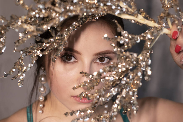 sexy attractive brunette woman in elegant green aquamarine dress with artificial branch with sparkly sequins. beautiful sensual girl. copy space. - 写真・画像