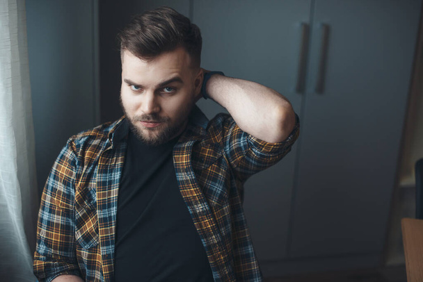 Bearded caucasian man is touching his head posing pensive at home looking at camera - Photo, Image
