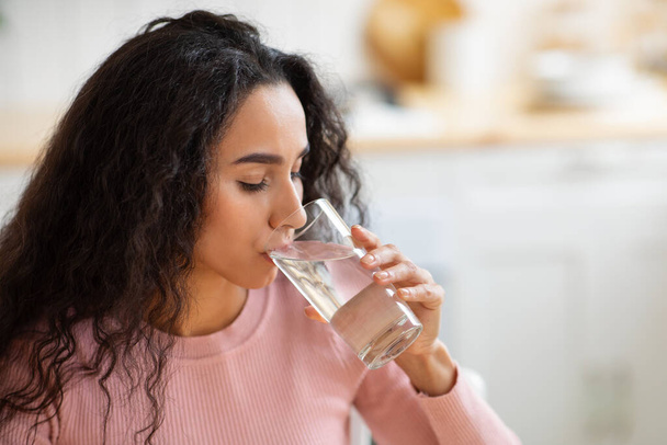 Υγιές υγρό. Όμορφη γυναίκα Brunette πόσιμο μεταλλικό νερό από γυαλί στην κουζίνα - Φωτογραφία, εικόνα