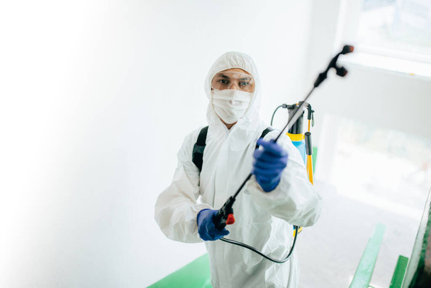Closeup shot of a sanitary professional worker wearing protective suit disinfecting a staircase entryway block of flats. Coronavirus prevention at living areas. New normal and stop Covid-19 spread - Photo, Image