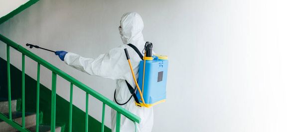 Breed schot. Sanitair professioneel werker in beschermend pak desinfecteert een trappenhuisblok van flats. Maatregelen ter voorkoming van het coronavirus in woonwijken. Nieuw normaal en stop Covid-19 spread - Foto, afbeelding