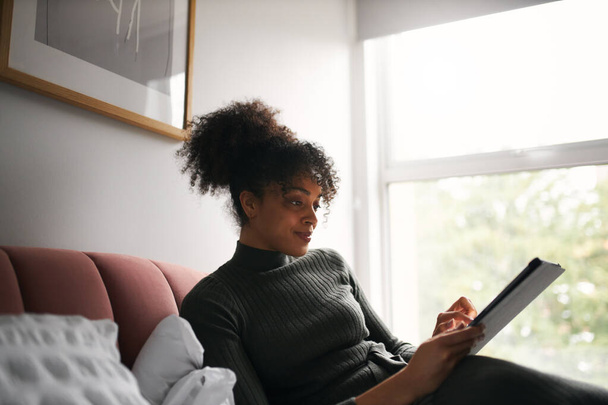 Mujer acostada en la cama leyendo o transmitiendo películas en tabletas digitales - Foto, Imagen